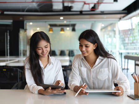 Portrait of two female university students doing homework together with digital devices in libraryの写真素材