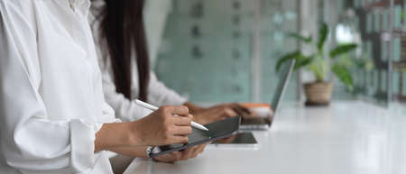 Side view of female hands using digital devices while sitting beside each other in co working space