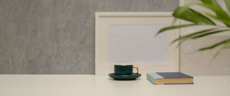 Close up view of worktable with cup, book, mock up frame, plant vase and copy space in living room