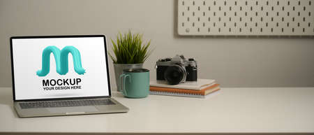Close up view of workplace with mock up laptop, camera, notebooks, mug, plant pot and copy space in home office roomの写真素材