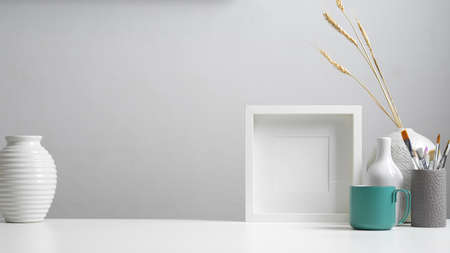 Close up view of home office desk with copy space, mock up frame, paint brushes and decorations in...