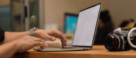 Side view of male photographer hands typing on mock up laptop on wooden table in studio
