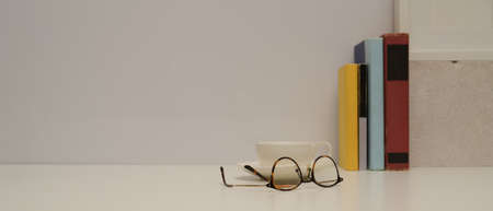 Close up view of study table with eyeglasses, books, cup, decorations and copy space on white tableの写真素材