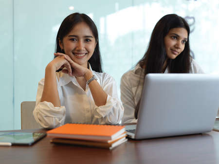 Portrait of two female university students in library while doing their assignment with books and laptopの写真素材