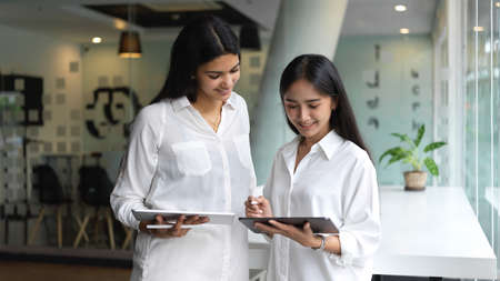 Portrait of two female office workers brainstorming on their project with digital tablet while standing in office roomの写真素材