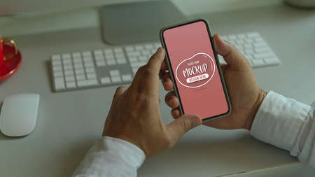 Close-up view of young businessman holding mock up smartphone in his office room