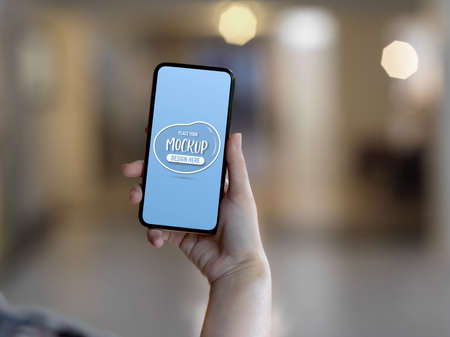 Close up view of female hand holding mock up smartphone in blurred background