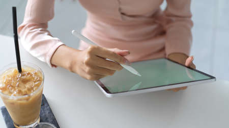 Close-up view of young woman writing on mock up tablet with beverage on the tableの写真素材