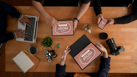 Top view of content creator team consulting on their project with mock up digital devices and camera on meeting tableの写真素材