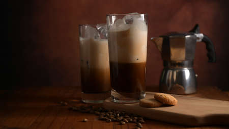 Close up view of Two glasses of ice coffee with biscuit on wooden tray, coffee pot and coffee beans...