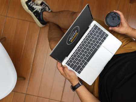 Top view of man relaxing in his room while holding mock up laptop computer and coffee cup