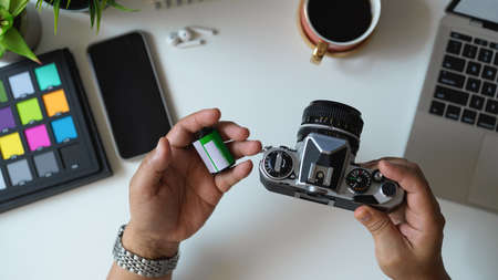 Top view of male photographer holding camera and camera film on his hand in workspace