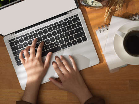 Top view of young woman typing on laptop computer on working table with coffee cup and office...