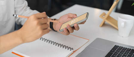 Cropped shot of businessman working on his idea with mock up smartphone while holding pencil to...