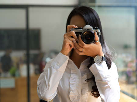 Portrait of female photographer taking photo with camera in studio