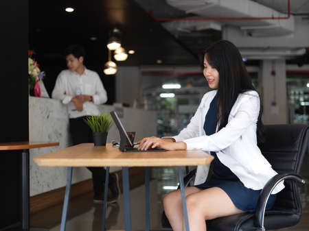 Young professional businesswoman working on her assignment while typing on tablet with her co-worker in the backgroundの写真素材