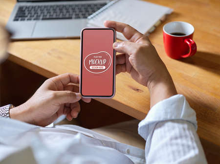 Close up view of male using mock up smartphone while sitting at worktable in office roomの写真素材