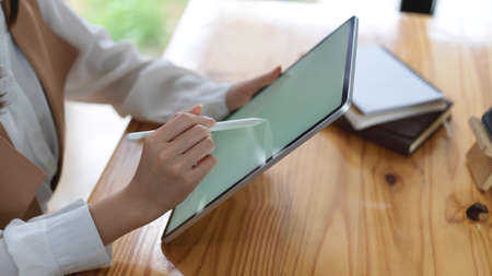 Side view of female student doing homework with mock up tablet on wooden table in cafe