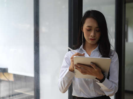 Portrait of female worker using digital tablet while standing in glass wall meeting room