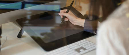 Close-up view of young designer working on her concept with graphic  tablet, view through glass view