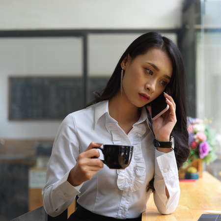 Portrait of female talking on the phone while drinking coffee in cafaの写真素材