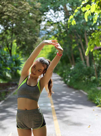 Young fit asian female athlete stretching her arms before exercise in the parkの写真素材