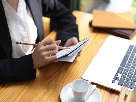 Cropped shot of businesswoman working with laptop and writing information on her notebook