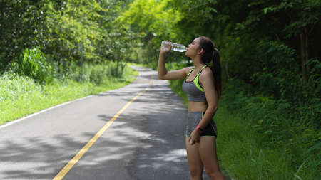 Young female athlete drinking water while exercise in the park