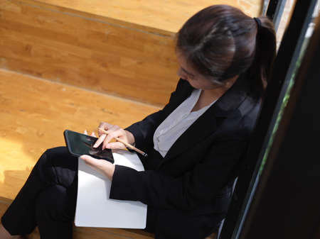 Overhead shot of businesswoman using smartphone while relaxed sitting at stair in officeの写真素材
