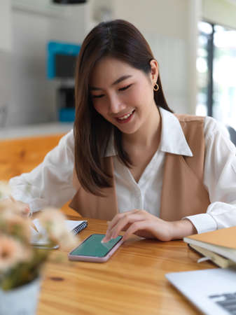 Portrait of female college student searching information on smartphone  while doing homework in cafeの写真素材