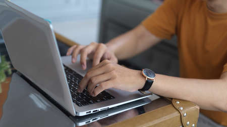 Cropped shot of hands typing on laptop keyboard on coffee table in living room