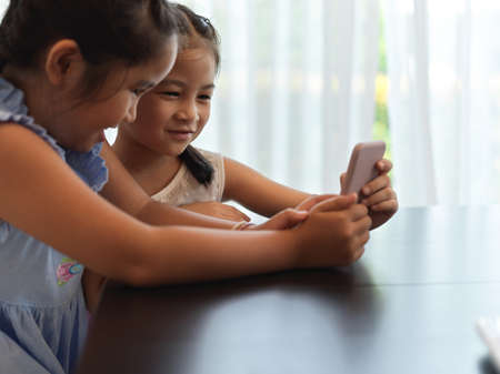 Side view of two girls playing with smartphone together on table in living room