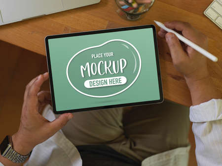 Overhead shot of male worker using mock up digital tablet on wooden table in office room