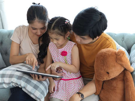 Portrait of family with father, mother and daughter homeschooling on digital tablet together while sitting on sofaの写真素材