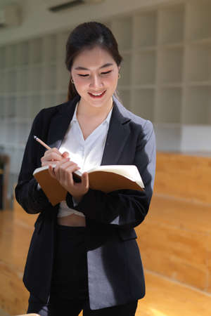 Portrait of businesswoman writing on schedule book while standing in office room