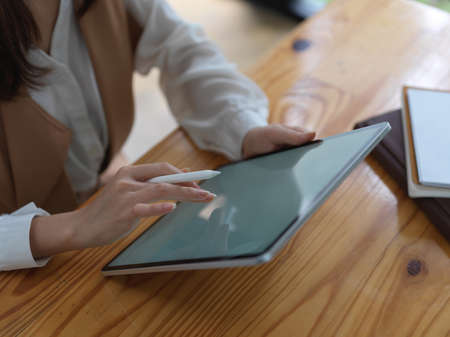 Cropped shot of female college student doing homework with mock up digital tablet on wooden desk