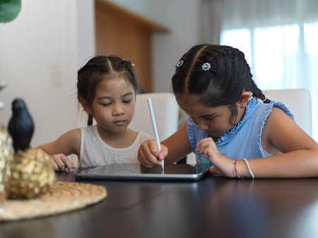 Portrait of two sisters using digital tablet together on table in living room