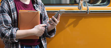 Cropped shot of female worker holding notebooks and using smartphone while standing in front of her...