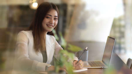 Portrait of female office worker smiling and looking into camera while working with stationery and...