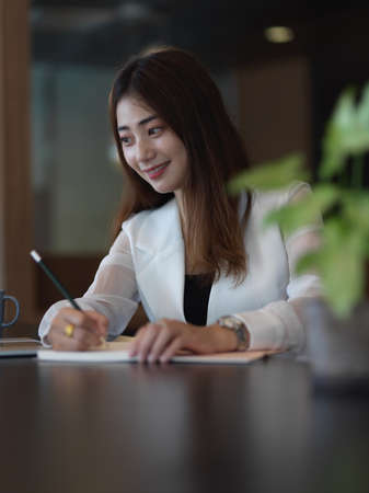 Portrait of female office worker working with stationery on table in office room