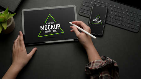Top view of female working on mock up digital tablet on black table with mock up smartphone and...