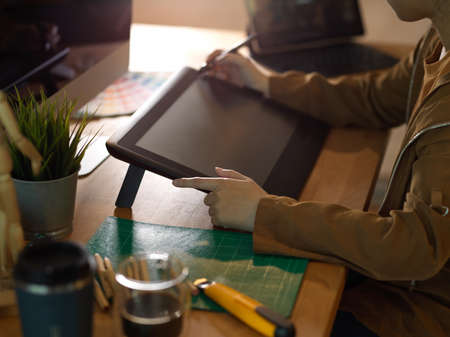Side view of female hands working with drawing tablet and computer on worktable in office roomの写真素材