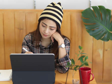 Portrait of female teenager working with digital tablet on wooden table with coffee mug and plant...
