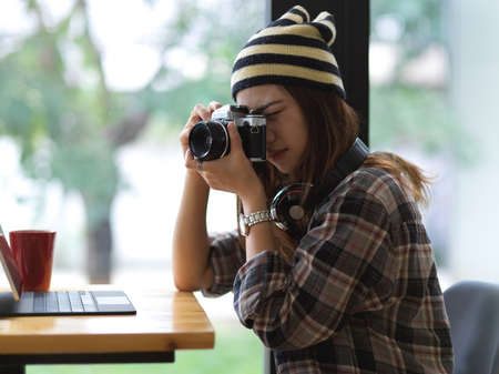 Portrait of female photographer taking photo with digital camera while sitting in cafe