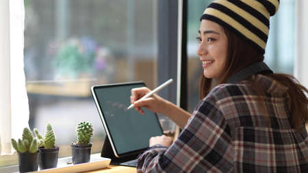 Side view of female teenager working with mock up tablet on wooden table in cafe