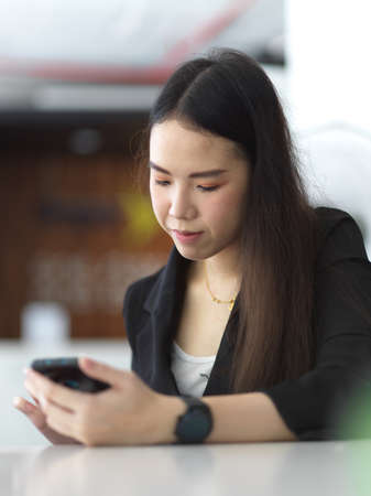 Portrait of young businesswoman texting on smartphone while relaxing in office room