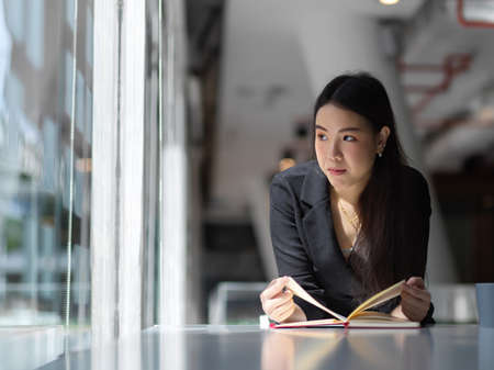Portrait of businesswoman looking trough glass wall while reading her schedule book