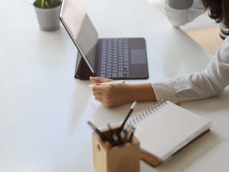 Side view of female hands working with digital tablet and notebook on white table