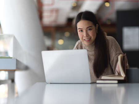 Portrait of female teenager studying with laptop and books on white table in co working spaceの写真素材