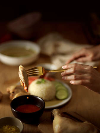 Close-up view of woman eating Hainanese chicken rice (steamed chicken rice), dipping chicken in the...
